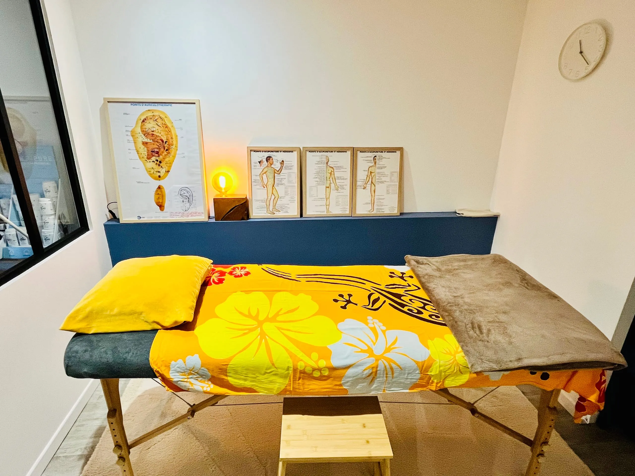 Cabinet de soin lumineux avec table de massage, coussins colorés et schéma d’auriculothérapie