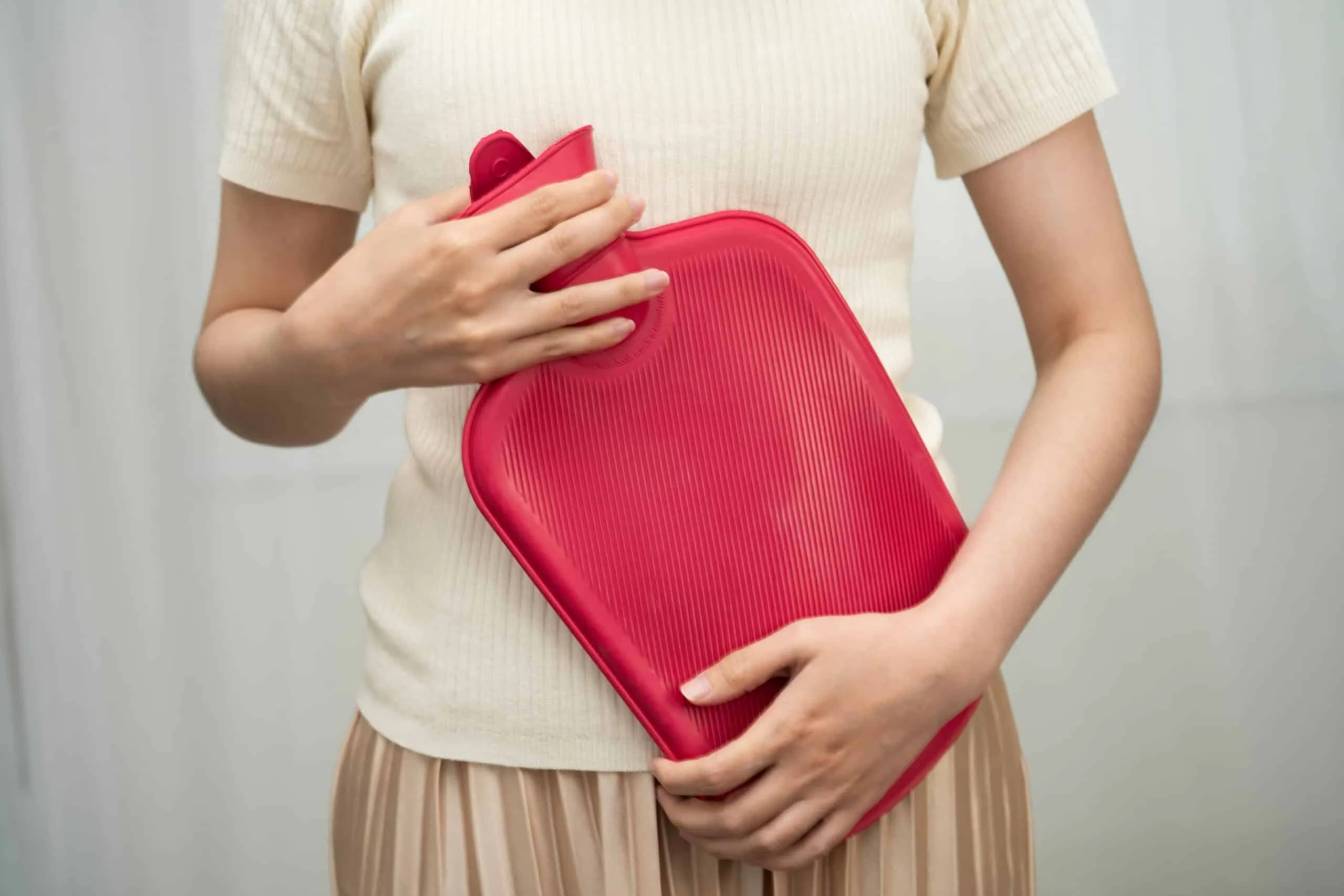 Femme tenant une bouillotte rouge sur son ventre