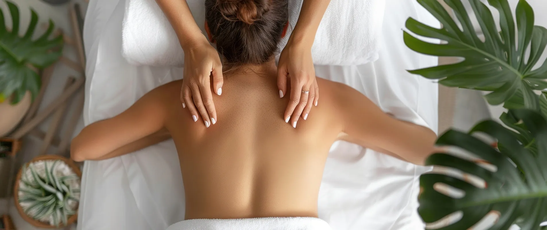 Massage du haut du dos sur une table de soin, avec serviettes blanches et plantes vertes.