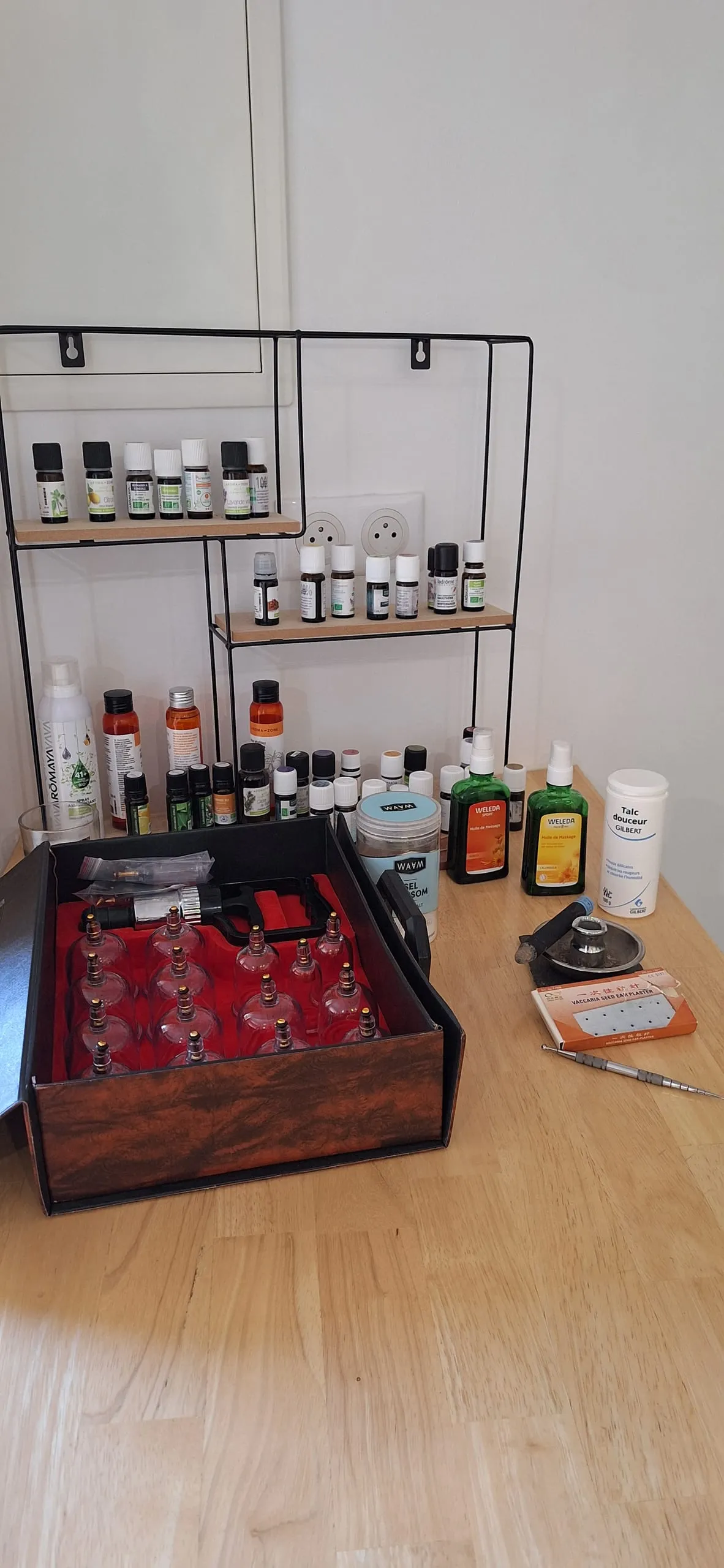 Plan de travail en bois avec coffret de ventouses en verre, étagères d’huiles essentielles, huiles de massage et brûleur de moxibustion.
