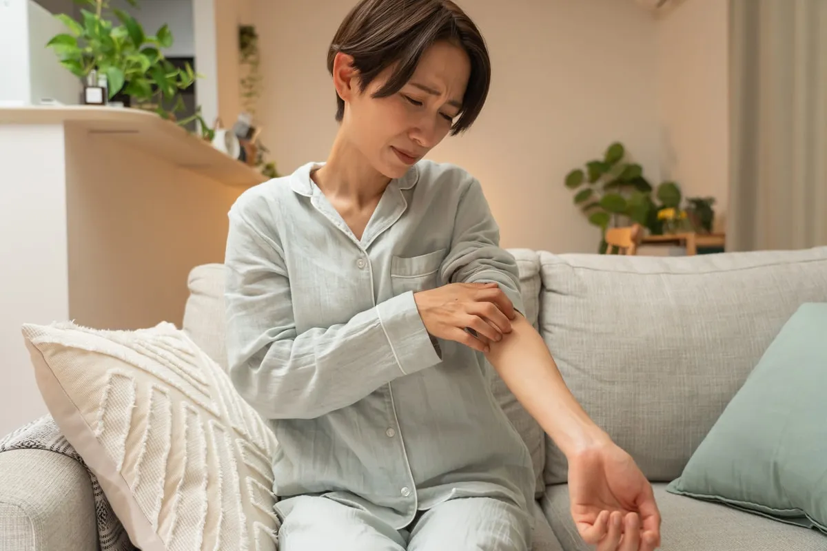 Femme assise sur un canapé se grattant l’avant-bras