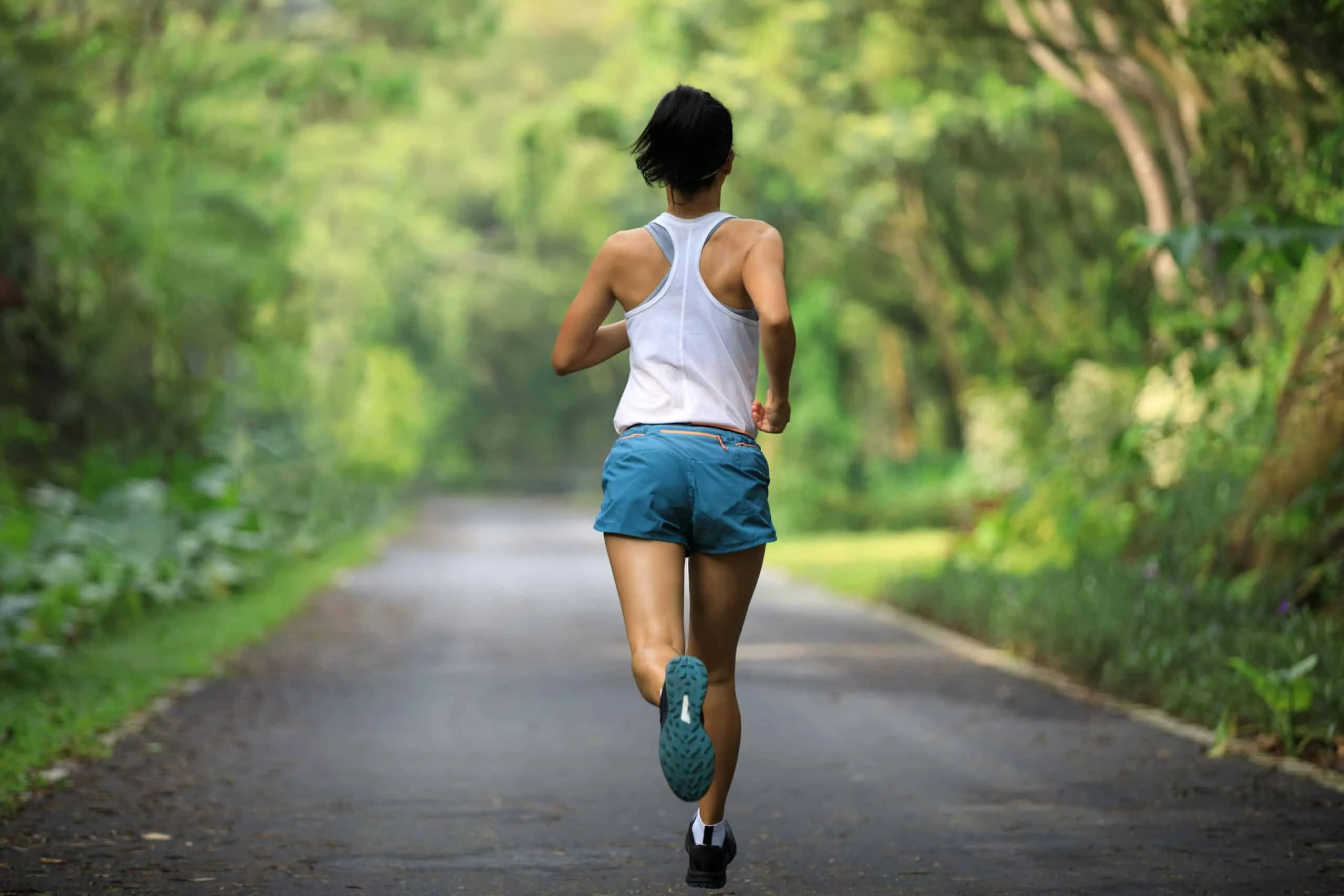 Femme en tenue de sport courant sur un chemin bordé d’arbres