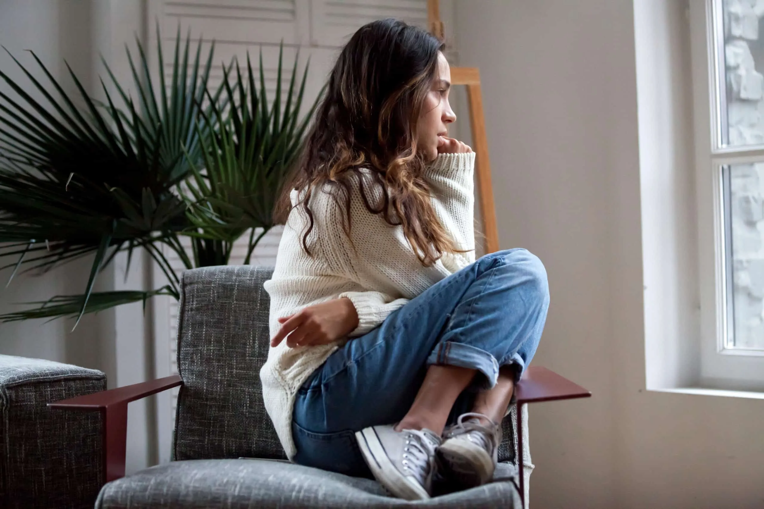 Femme pensive assise dans un fauteuil et regardant par la fenêtre