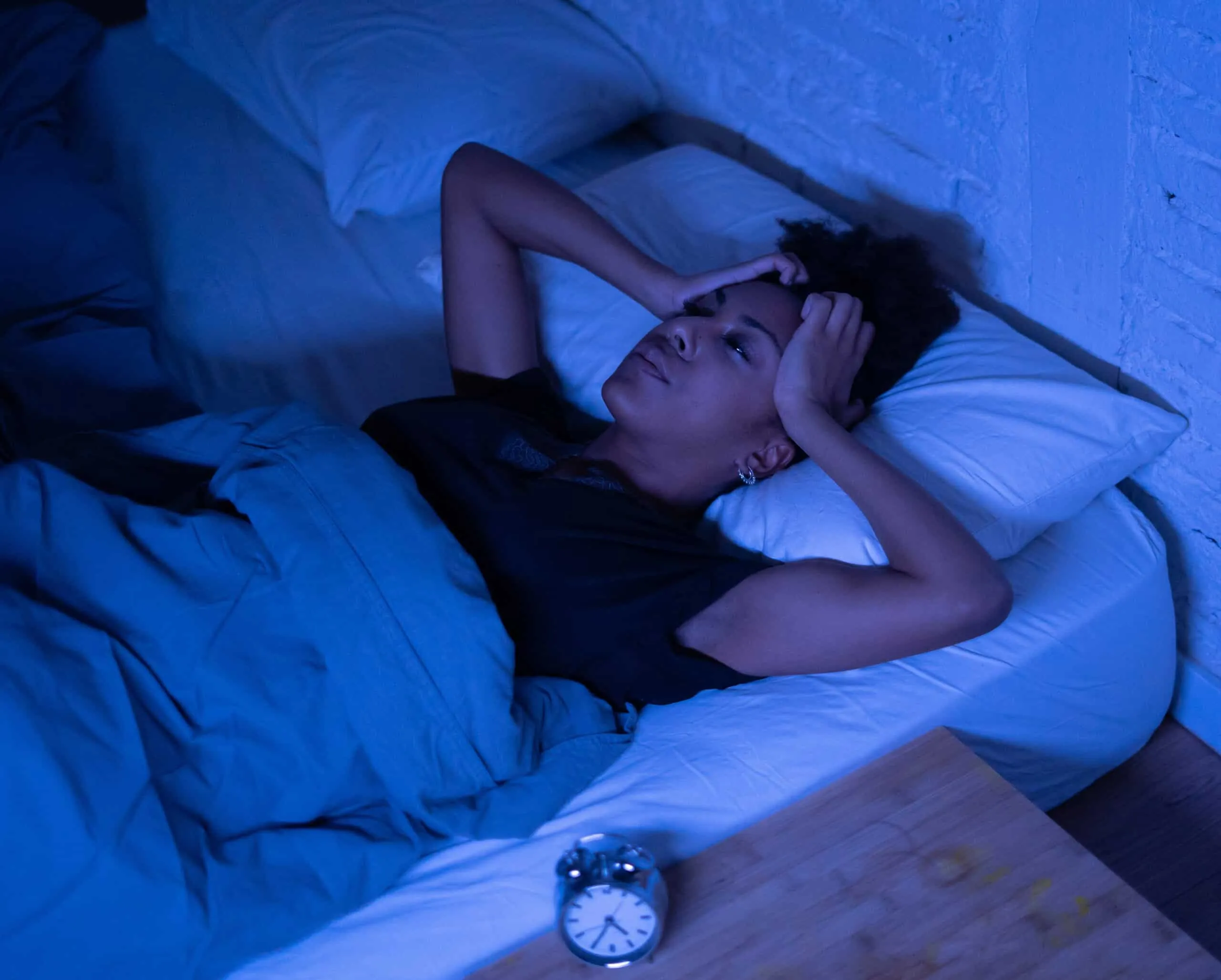 Femme éveillée dans son lit la nuit, les mains posées sur la tête